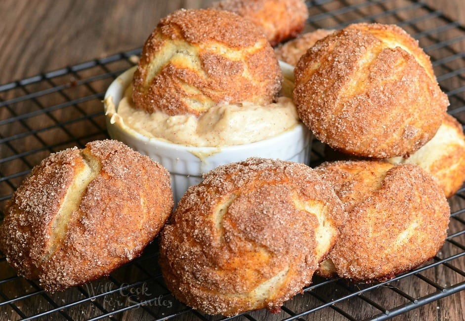 Snickerdoodle Pretzel Puff on a cooling wrack with on of the puffs in a bowl of cinnamon butter