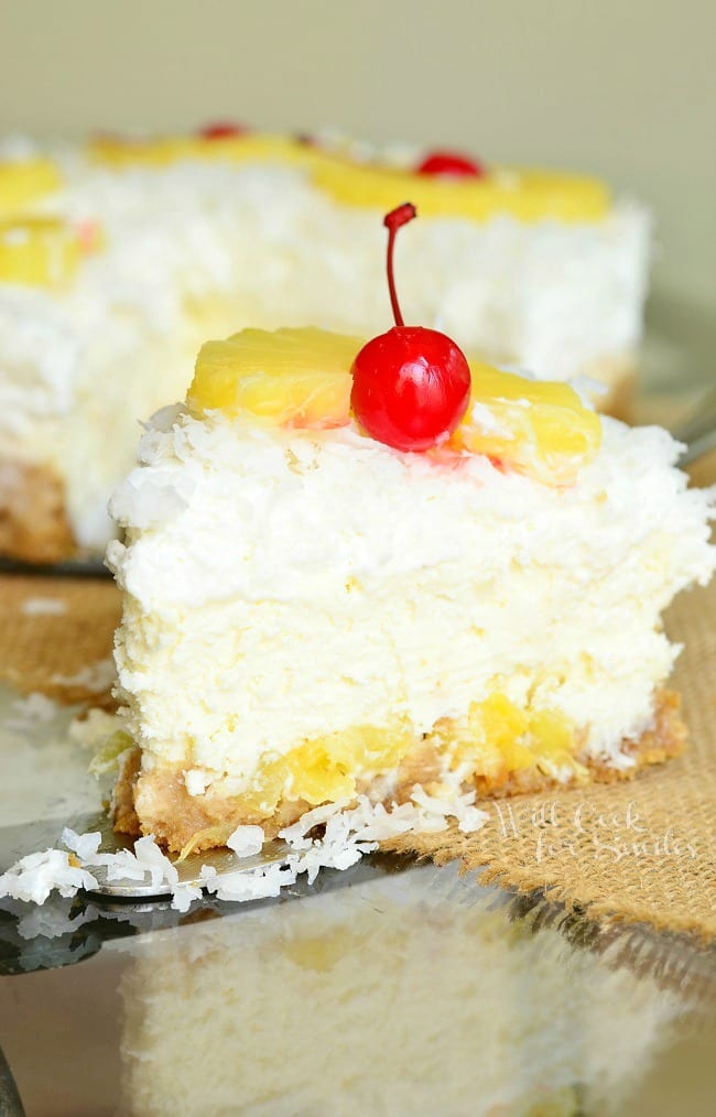 a slice of Pina Colada Cheesecake with a piece of pineapple and a cherry on top