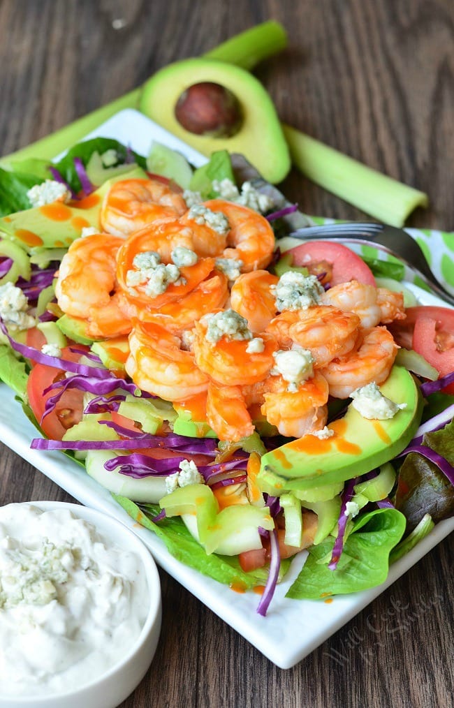 white bowl with homemade blue cheese dressing and a buffalo shrimp salad on a wooden table as seen from above
