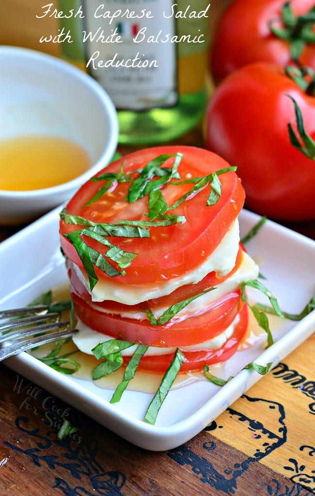 small white square plate with fresh caprese salad with a bottle of oil and additional tomatoes in the background