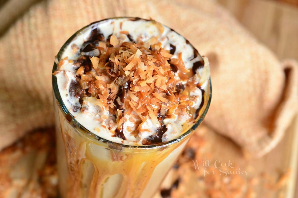 top view photo of Samoas Frozen Coffee in a glass cup with whip cream, toasted coconut, chocolate sauce, and caramel on top. Caramel and chocolate sauce pouring down the outside of the glass