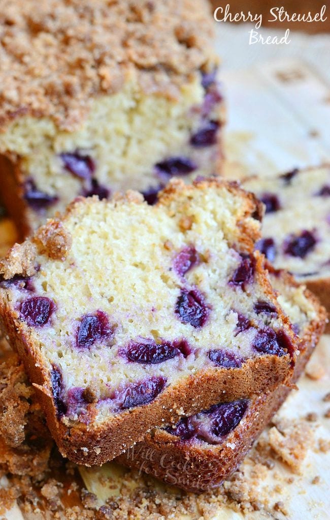 A few pieces of Cherry Streusel Bread have been cut from the loaf. The cut pieces lay stacked on each other in front of the loaf. The streusel is on top of the bread and laying around the bread slices.