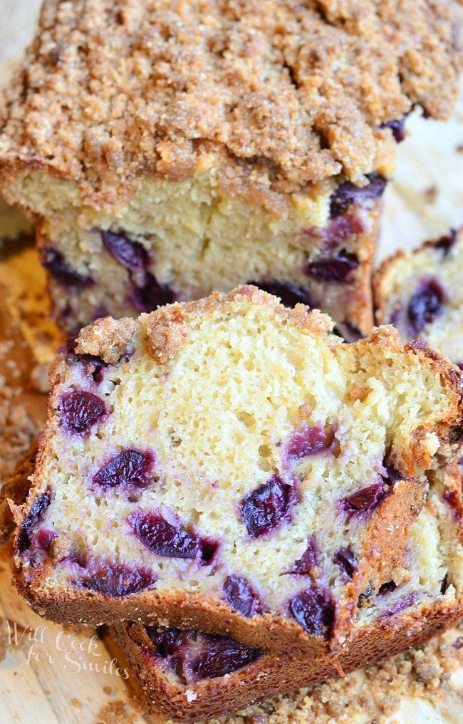 A few pieces of Cherry Streusel Bread have been cut from the loaf. The cut pieces lay stacked on each other in front of the loaf. The streusel is on top of the bread and laying around the bread slices.