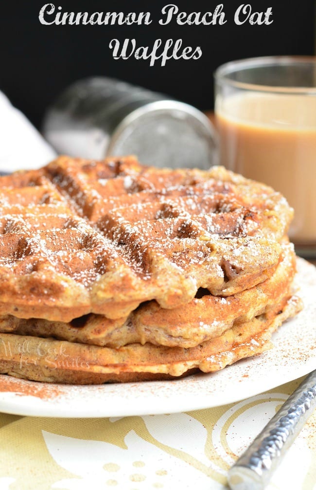 Three Cinnamon Peach Oat Waffles stacked on top of each other served on a white plate. Waffles are sprinkled with cinnamon and powder sugar.