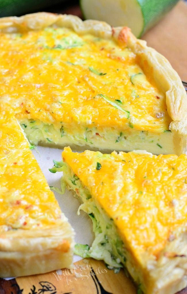close up view of 1 slice seperated from sriracha zucchini and cheese quiche on a wood table as shown from above