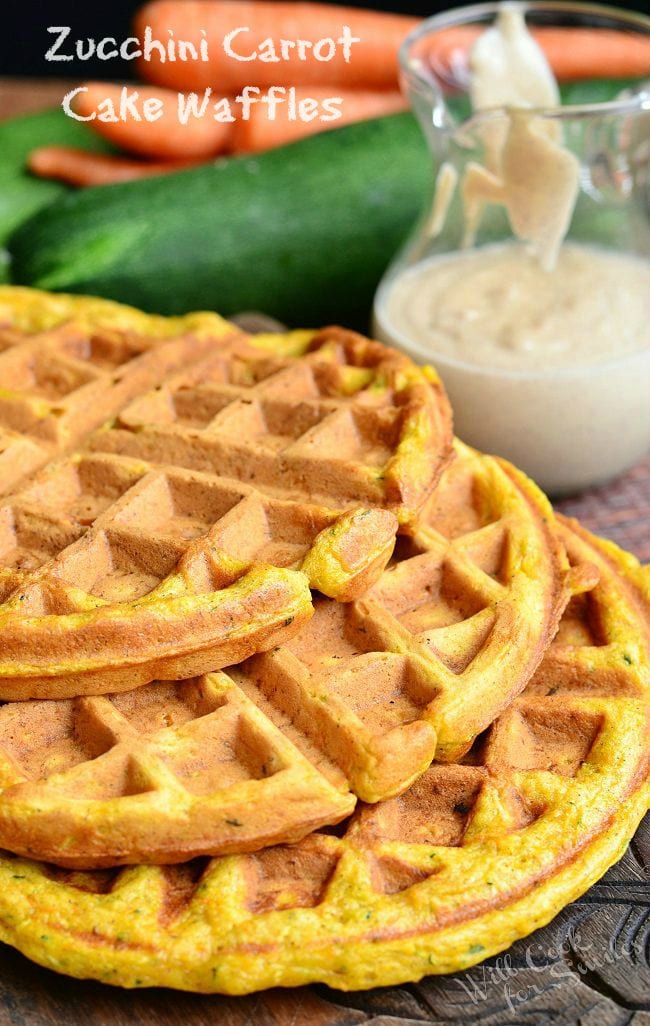 3 zucchini carrot cake waffles stacked on a wooden cutting board