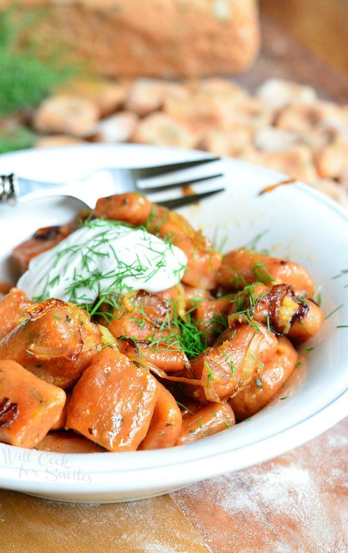 close up photo of Tomato Herb Gnocchi cooked in a white bowl with sour cream and dill on top and a fork to the back of the bowl on a wood table