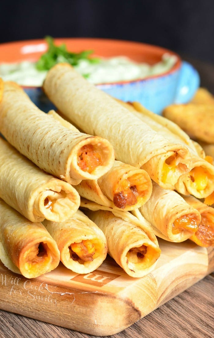 Avocado Ranch Dip in a bowl with Jose Ole Taquitos on a cutting board