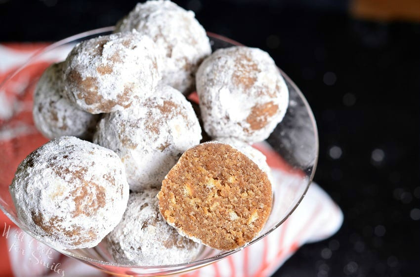 Decorative martini glass filled with pumpkin spice rum balls asviewed from the top with one ball cut in half with a red and white cloth in the background viewed close up