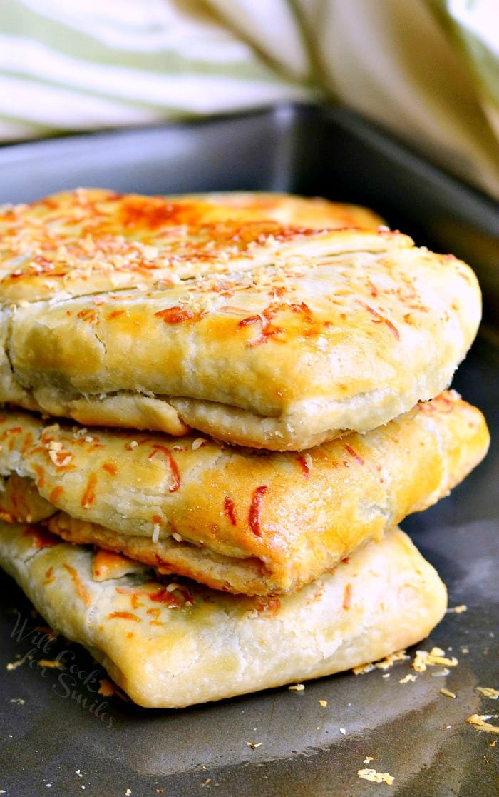 Spinach Artichoke Hand Pies stacked up on a baking sheet