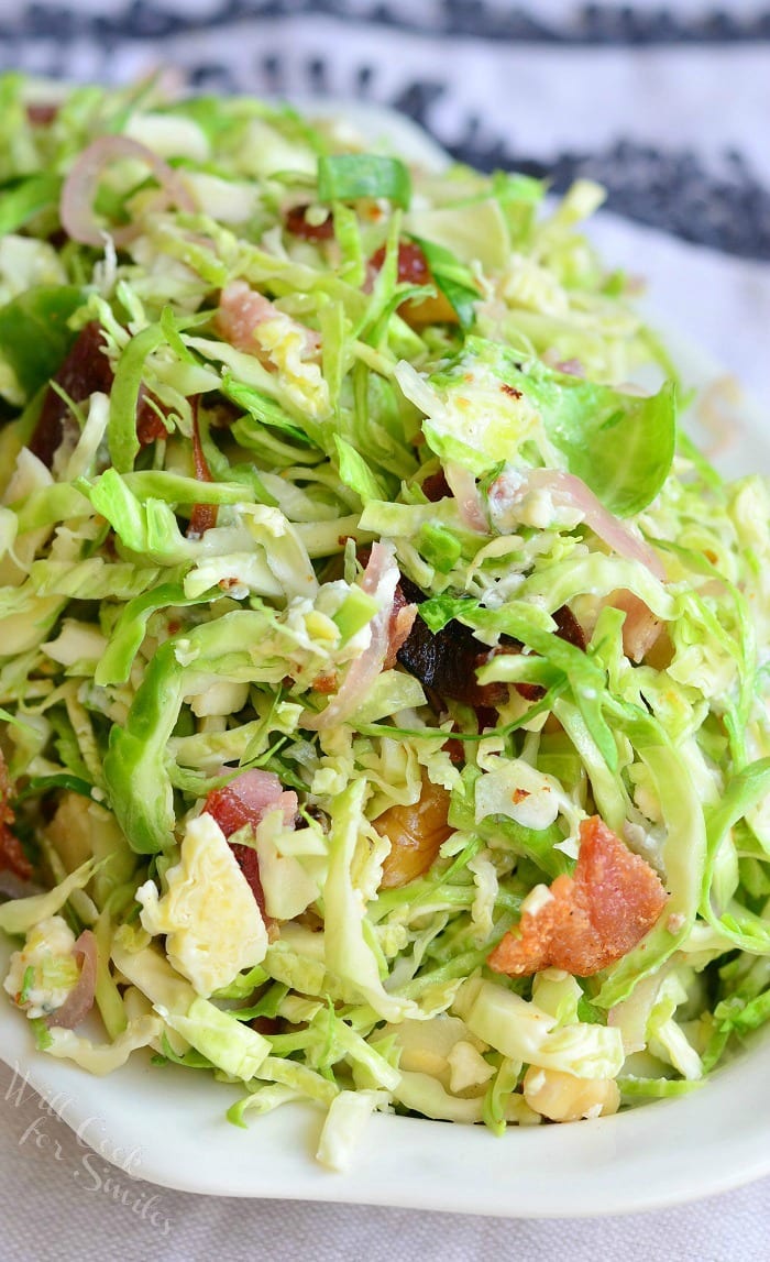 small white bowl filled with a bacon and blue brussels sprouts salad with warm bacon vinaigrette on a white table cloth covered table