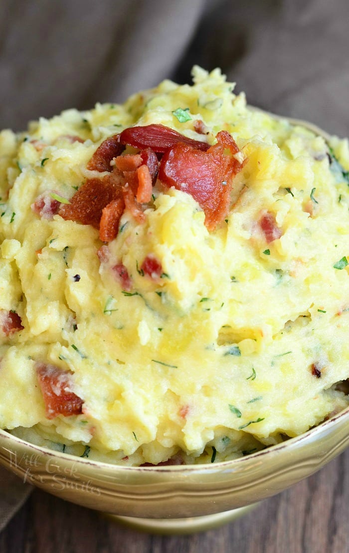 Mashed Potatoes with bacon and herbs mixed in and bacon on top in a bowl