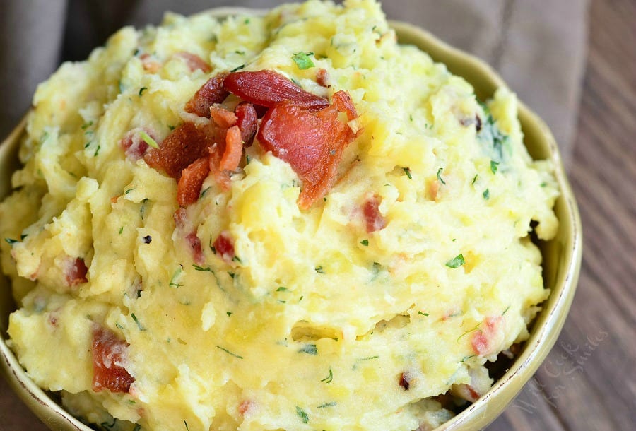 small decorative bowl filled with bacon and herbs creamy mashed potatoes on a wooden table as viewed from above and close up