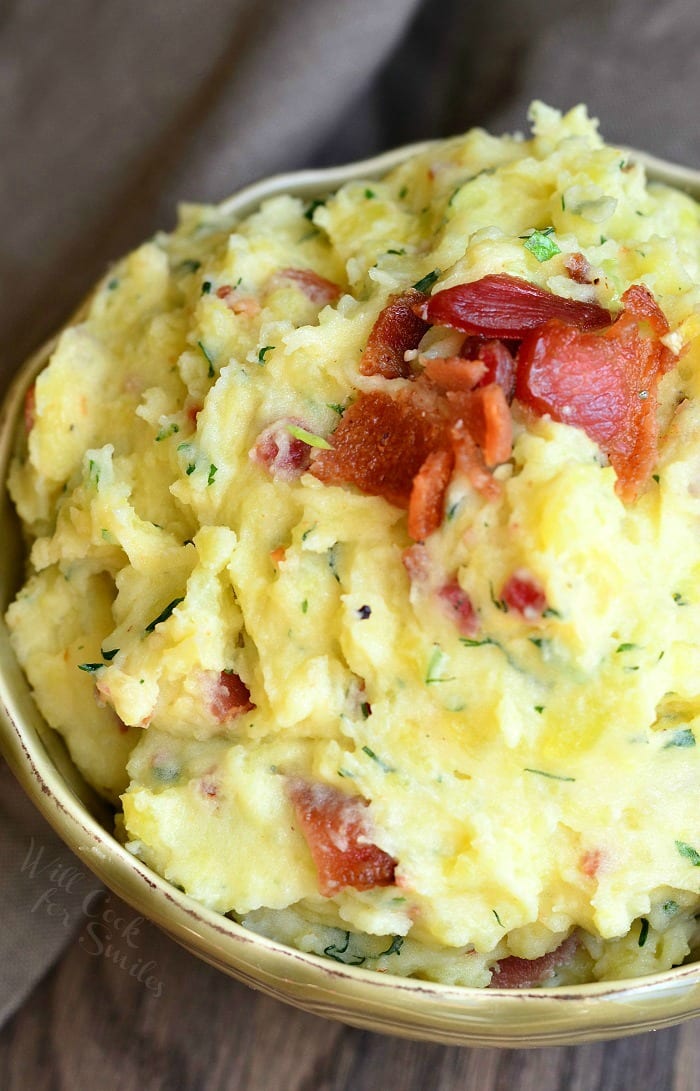 Mashed Potatoes with bacon and herbs mixed in and bacon on top in a bowl