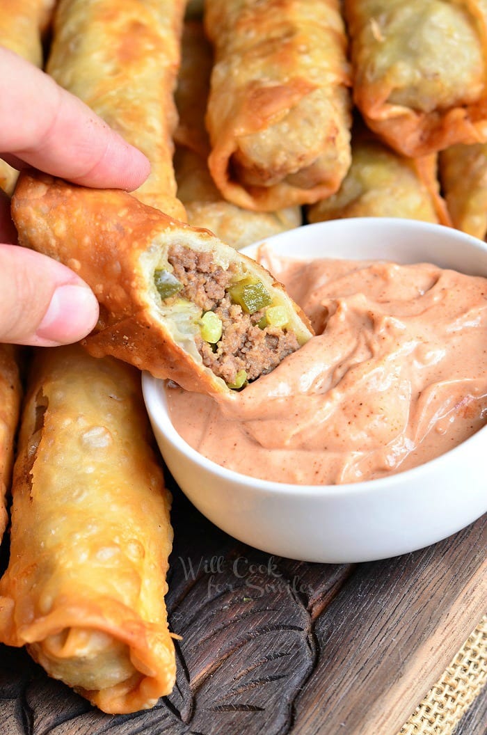 Cheeseburger Egg Rolls being dipped sauce that is in a white bowl