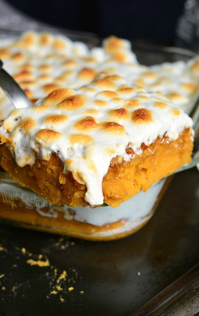 1 portion of sweet potato casserole cake being held above the rest of the cake in a glass baking pan on a black pan