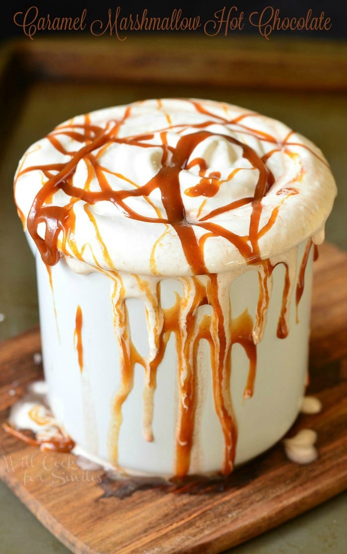 Metal dessert mug filled with caramel marshmallow hot chocolate on a wooden table covered in caramel drizzle