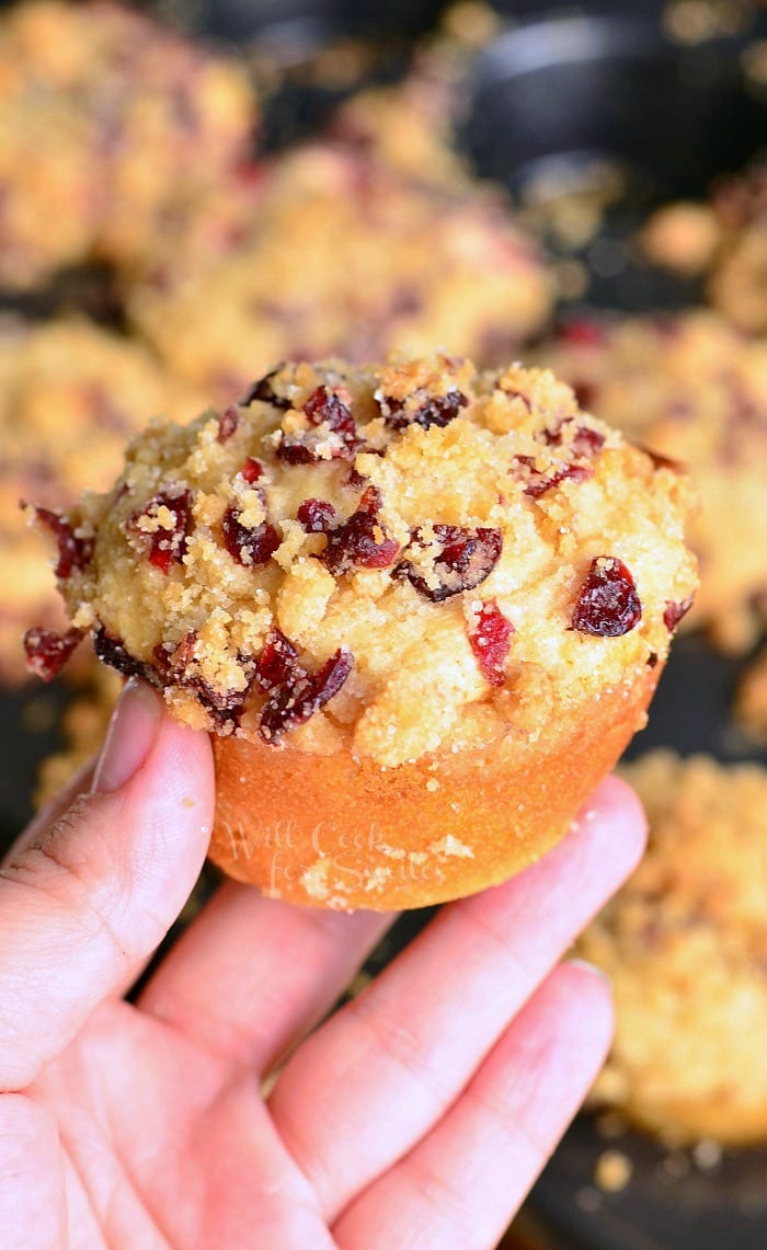 hand holding 1 cranberry white chocolate chip streusel muffin above more muffins