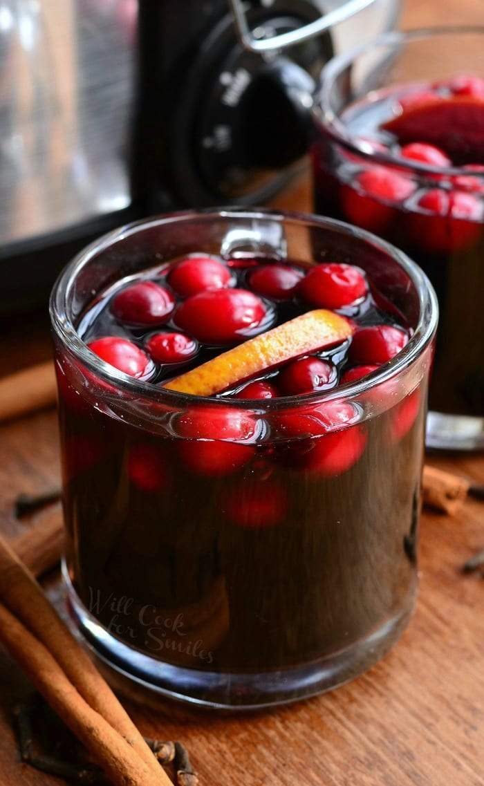 Orange Cranberry Sangria in a glass mug with orange and cranberries inside on a table with cinnamon sticks around it