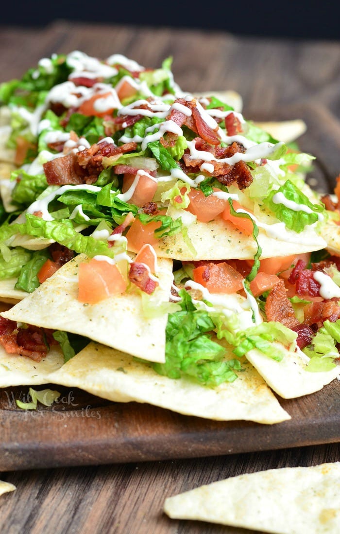 BLT Nachos with lettuce, tomato, and bacon, on a wood cutting board