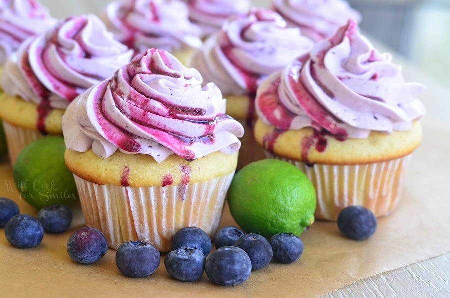 Cupcakes with Fresh Blueberry Cream Cheese Frosting on a cutting board with blueberries and limes