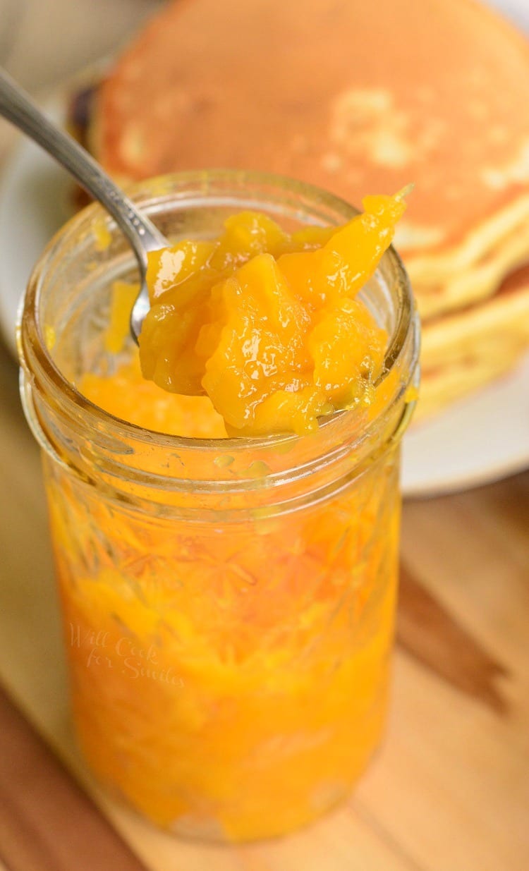 Mango jam in a glass jar with pancakes in the background
