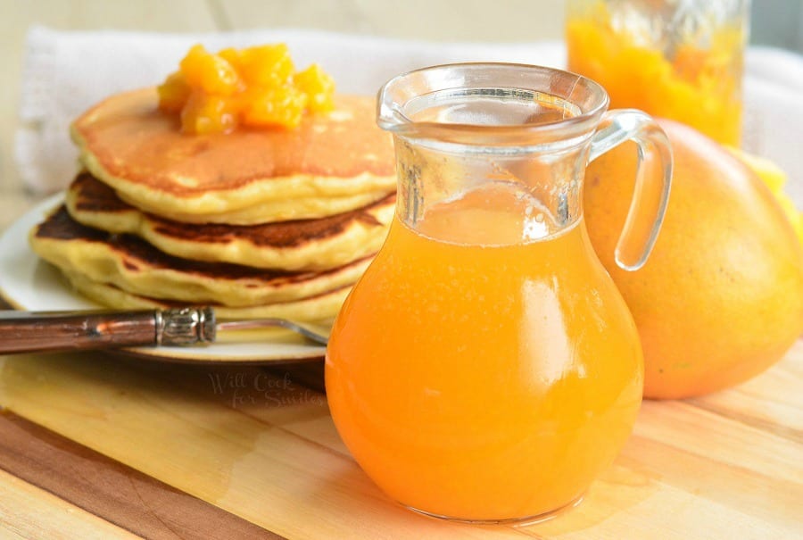 mango syrup in a jar and pancakes on a plate with mangos on top and a fork across the front of the plate