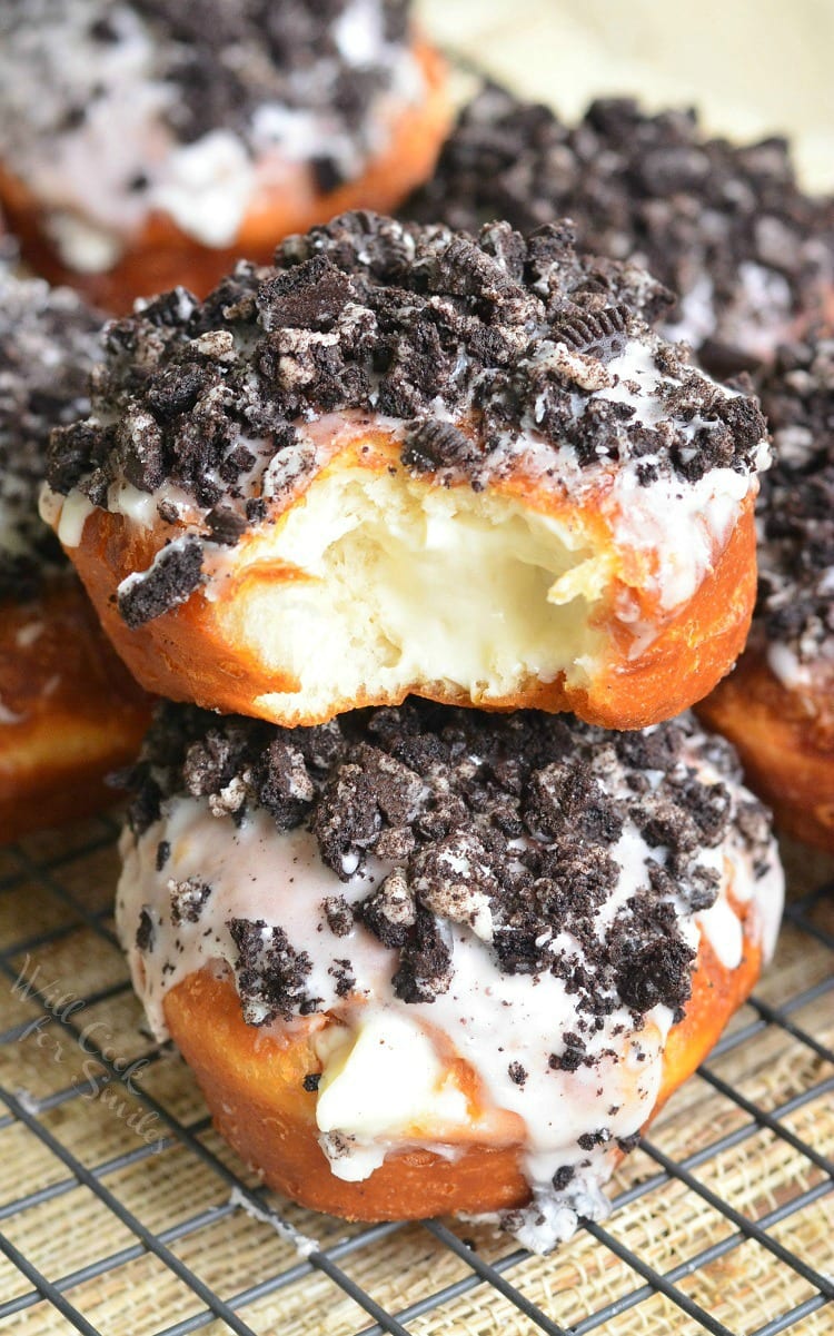 Oreo Cheesecake Doughnuts with crushed oreos with a bite missing on a cooling wrack