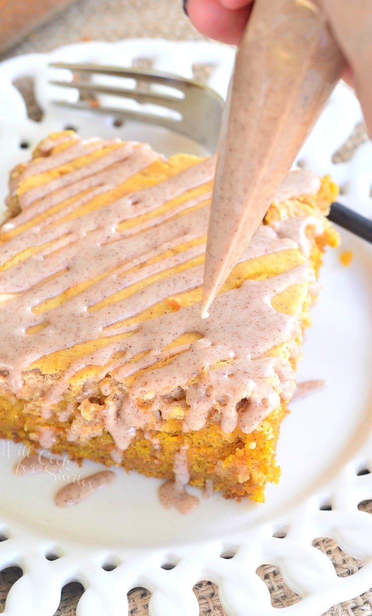 piping cinnamon icing on the Spiced Cheesecake Swirled Carrot Cake that is on a white plate