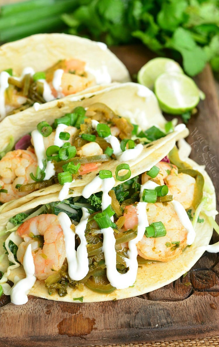 tequila lime shrimp tacos with sour cream drizzled on top on a cutting board