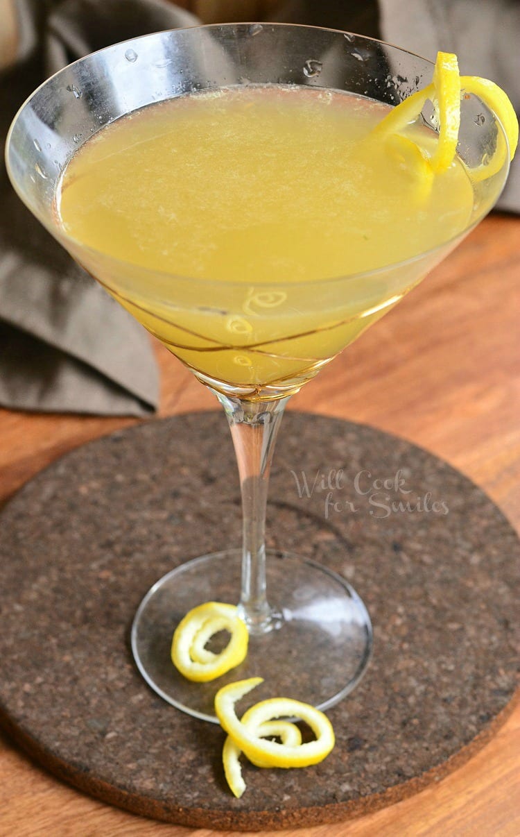 Decorative martini glass filled with pineapple lemon martini with lemon peel garnishes on the rimand around the stem of the glass as viewed from above
