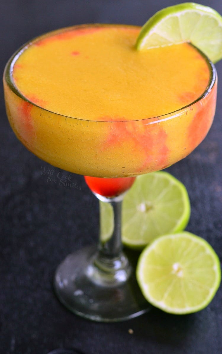 Sunset Margarita that is orange with some red in a margarita with a lime in it