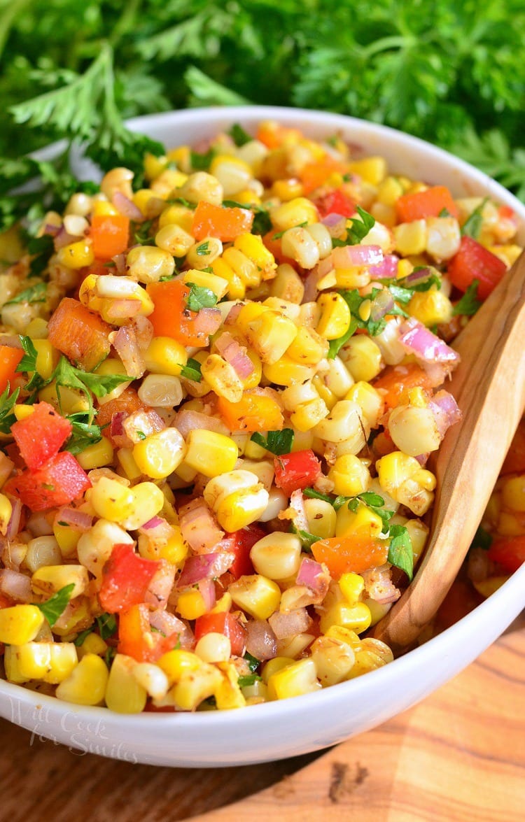 Cajun Corn Salad with corn, tomato, red onion, cilantro, and red peppers in a white bowl with a wood spoon