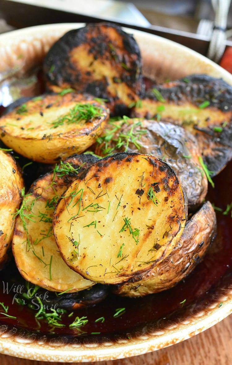 Herbed grilled potatoes on a brown and white platter on a wooden table topped with dill