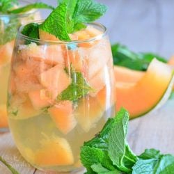 2 glasses filled with melon mint wine spritzer topped with mint leaves on a wooden table as viewed close up