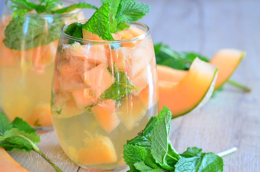 2 glasses filled with melon mint wine spritzer topped with mint leaves on a wooden table as viewed close up