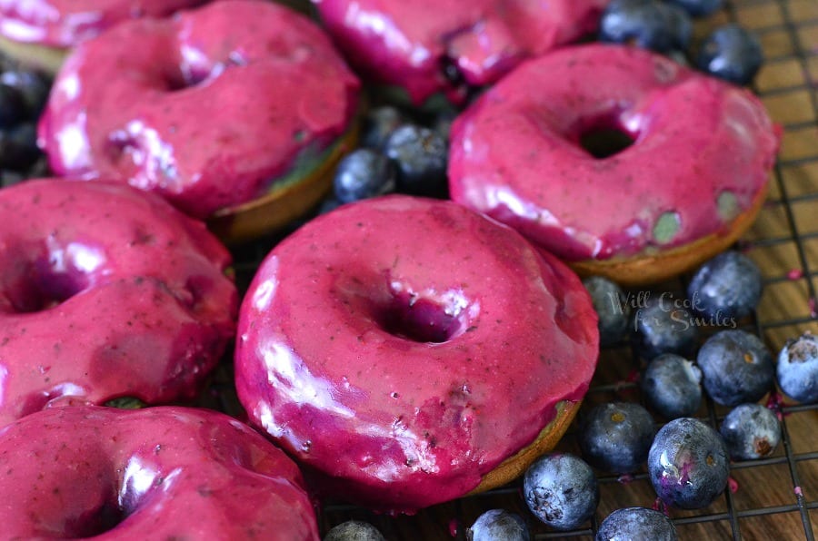 Blueberry Doughnuts with Blueberry Cream Whiskey Glaze on a cooling rack with blueberries on a wood table