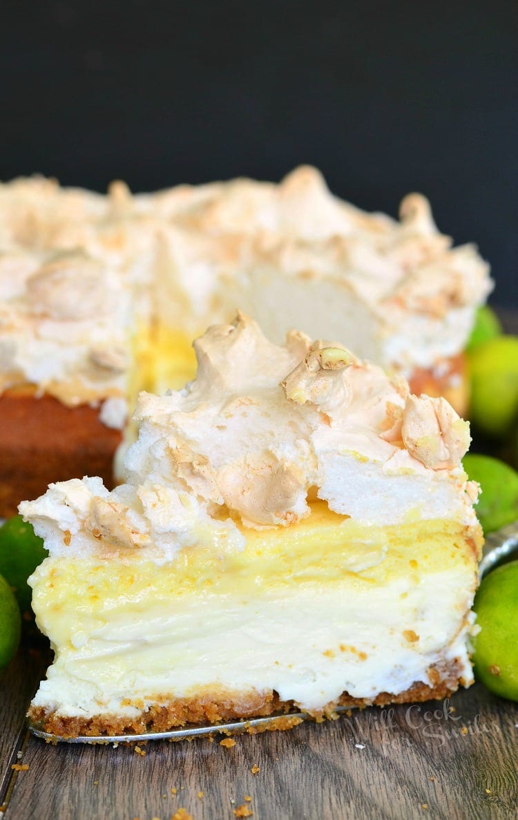 Slice of Key Lime Pie Cheesecake with meringue on top on a table with limes