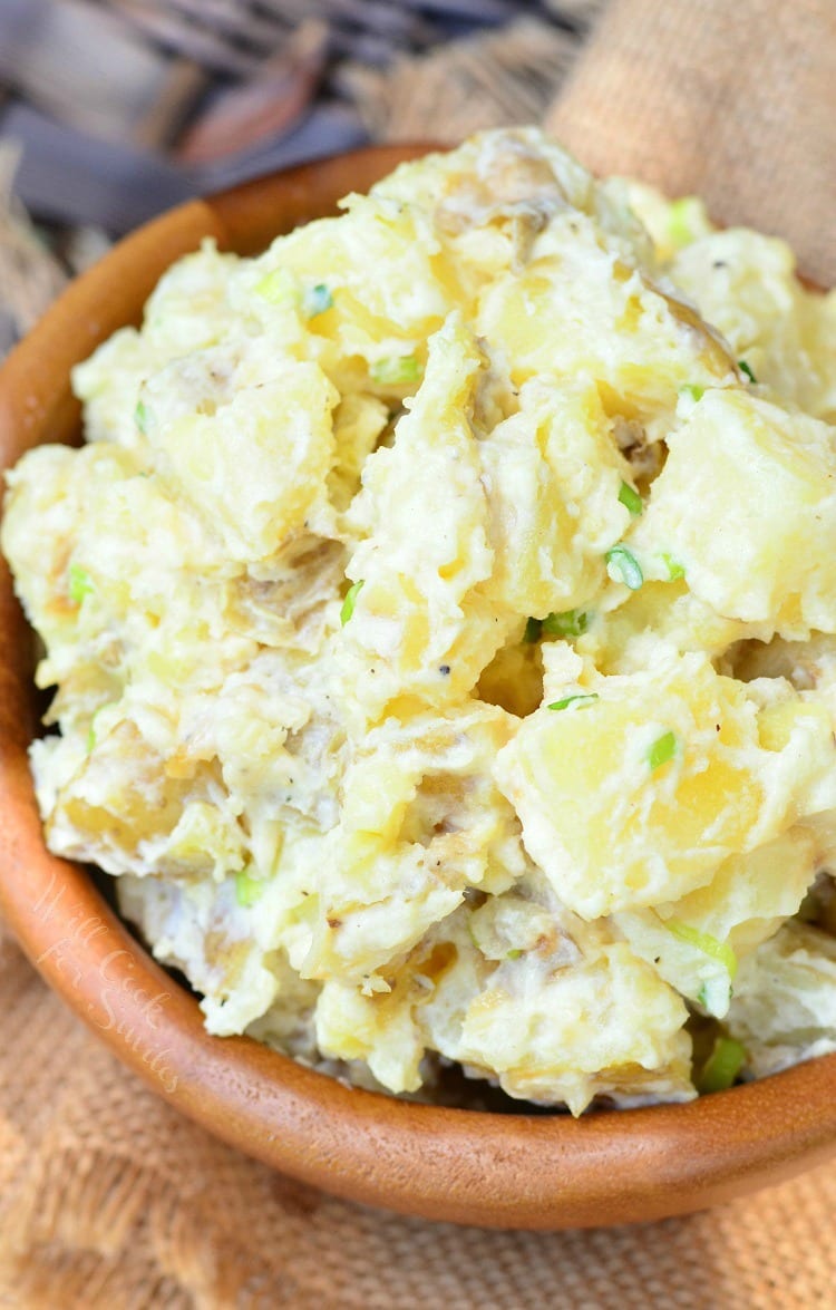 Wooden bowl filled with roasted garlic asiago potato salad on a tan cloth as viewed from above