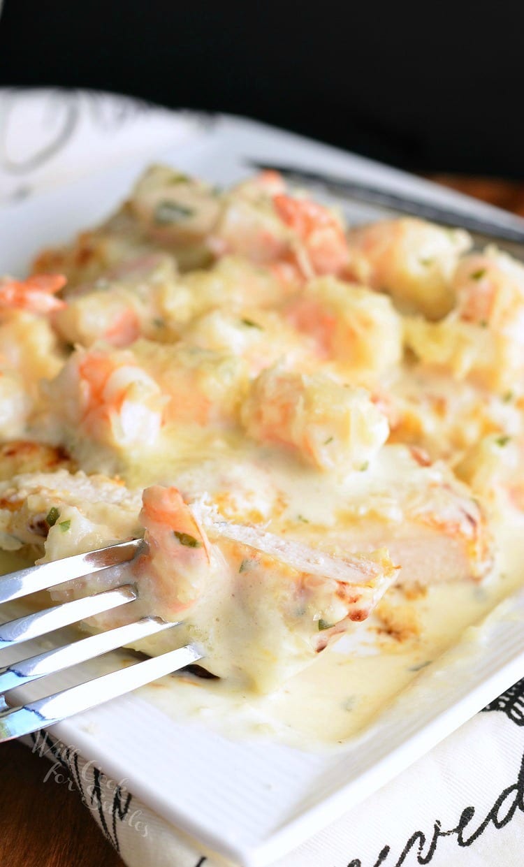 Oven Fried Chicken topped with shrimp and a Creamy Fontina cheese Shrimp Sauce on a white plate with a fork in a piece to the left
