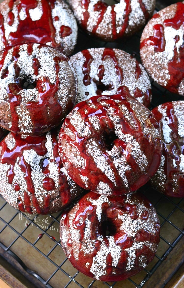 Raspberry Chocolate Doughnuts on a cooling rack with powdered sugar and raspberry sauce over the top of them on a cooling rack