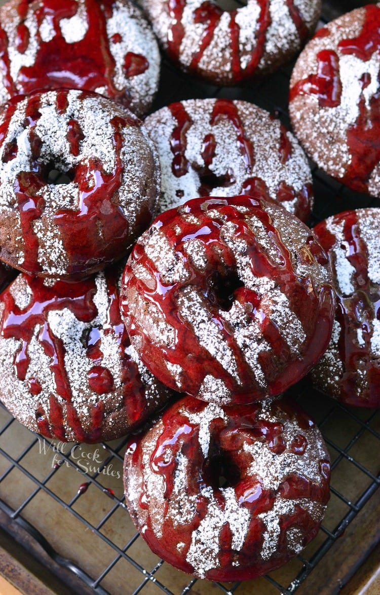 Raspberry chocolate doughnuts on a wire cooling rack topped with powdered sugar and raspberry glaze as viewed from above