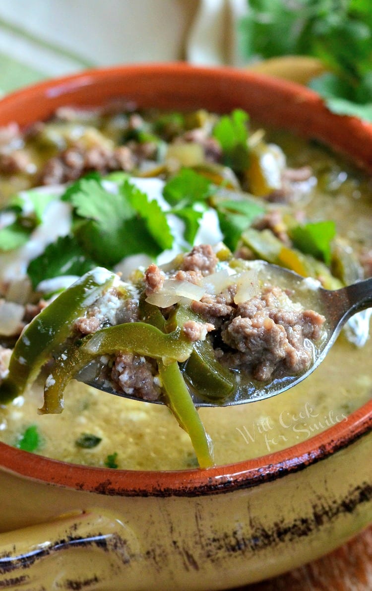 Ground beef with poblano peppers in a soup bowl with sour cream and cilantro on top with spoon lifting some out