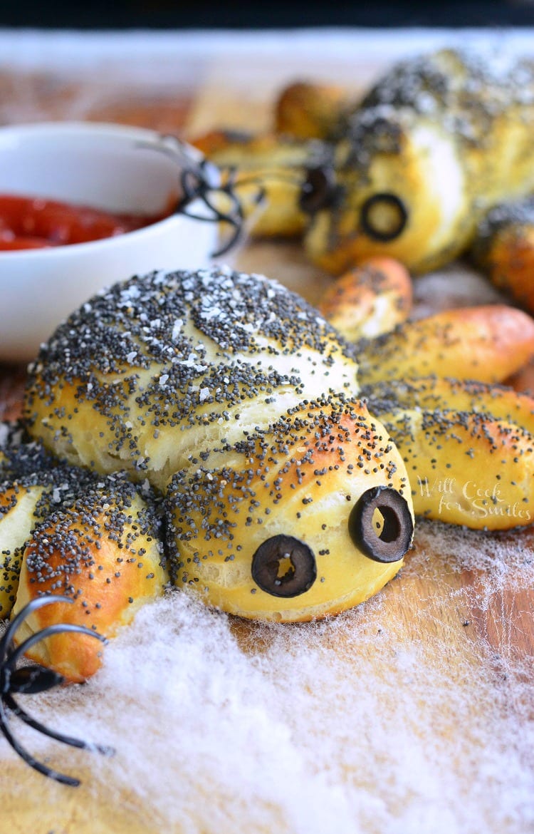 Decorative pretzel spiders on faux web and a wooden table with plastic spider rings around them.