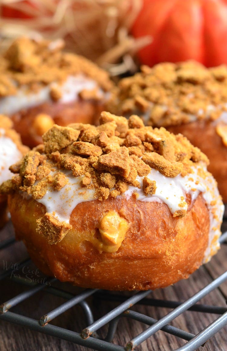 cheesecake pumpkin doughnuts with gingersnap crumb topping on a wire rack resting on a wooden table as viewed close up.
