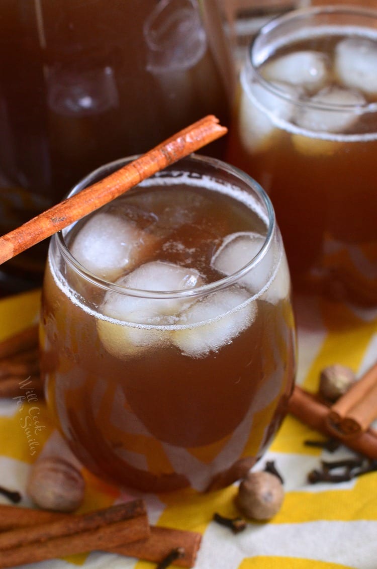 Glass filled with spiced iced tea with an additional glass and a pitcher filled with spiked tea in the background