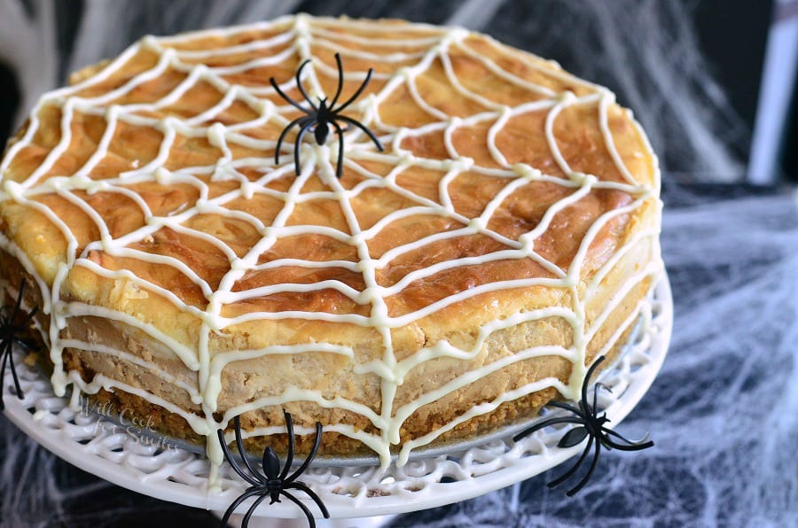 cheesecake on a white cake stand with spider web made out of frosting on it and 3 spiders