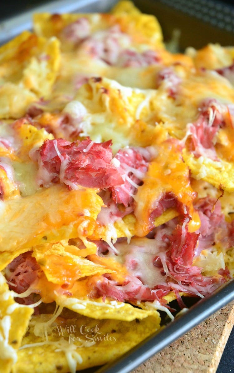 Tortilla chips, corn beef, and cheese on a baking sheet