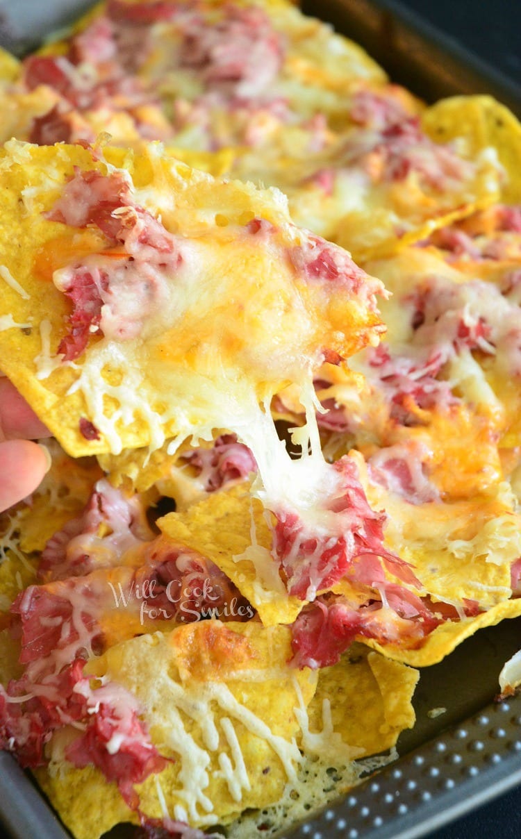 Baking sheet tray filled with reuben nachos with a hand pulling out 1 chip covered in toppings