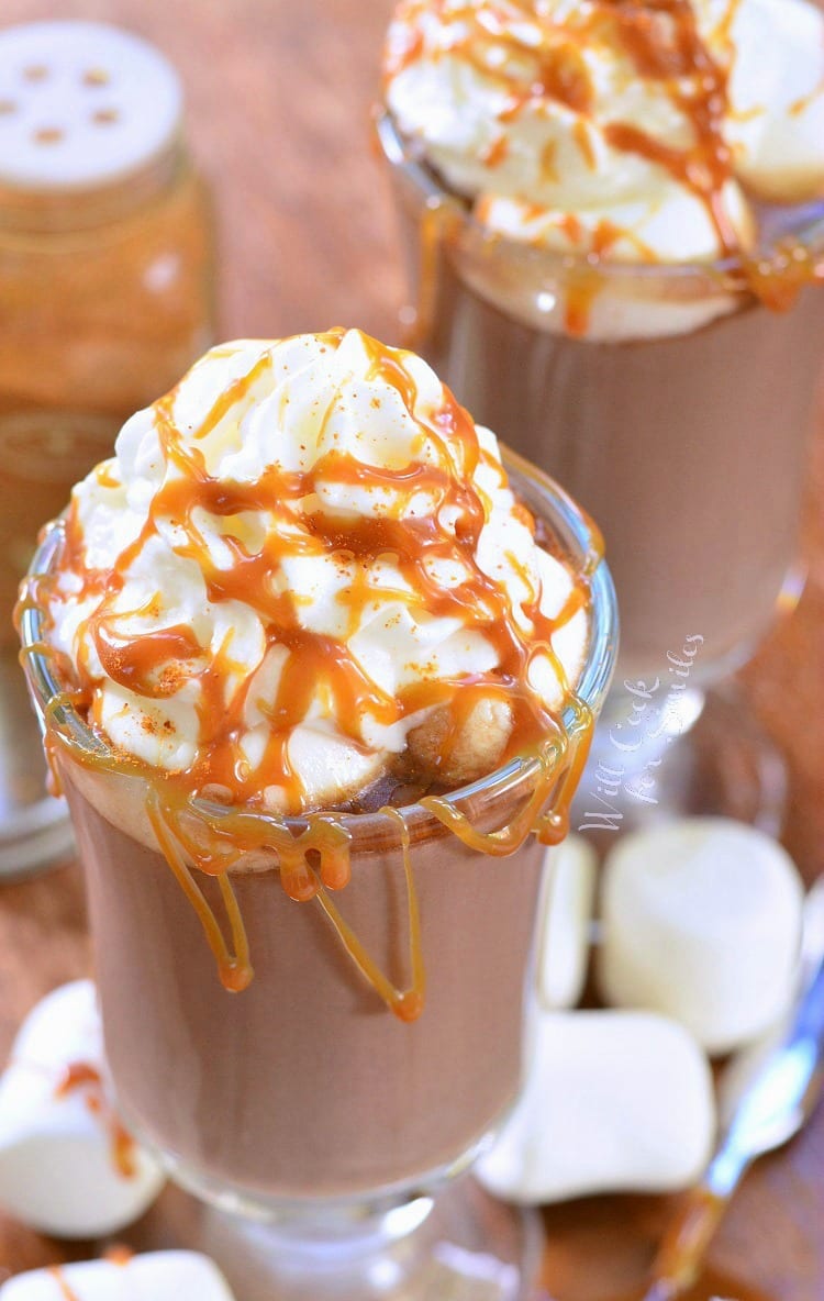 Dessert glass filled with caramel spicy hot chocolate on a wooden table with marshmellows around the base of glass as viewed from above